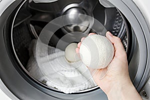 Woman using wool dryer balls for more soft clothes while tumble drying in washing machine concept