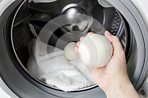 Woman using wool dryer balls for more soft clothes while tumble drying in washing machine concept photo