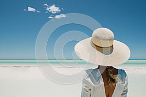Woman on vacation back view. Rear view of a young woman wearing a straw hat against a clean beach AI generation