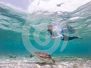 Woman on vacations wearing snokeling mask swimming with sea turtle in turquoise blue water of Gili islands, Indonesia