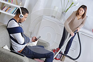 Woman vacuuming while man resting on couch