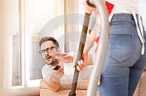 Woman vacuuming while man watching tv