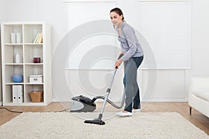 Woman vacuuming rug at home