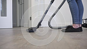 A woman vacuums the floor in the living room with a modern vacuum cleaner