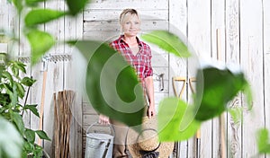 Woman in vegetable garden with watering can on white wooden shed background with gardening tools