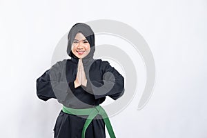 A woman in a veil in a pencak silat uniform poses respectfully with her hands cupped in front of her chest