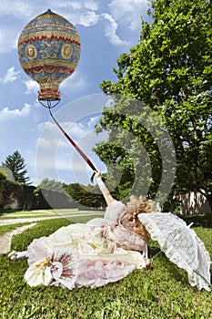 Woman in Venetian costume lying on the green park holding an old balloon