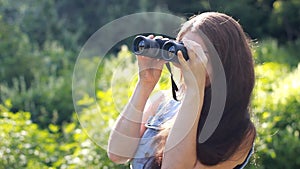 Woman with very long hair looks through binoculars outdoors on a windy summer day