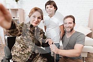 Woman veteran in wheelchair returned from army. The son and husband are happy to see her.