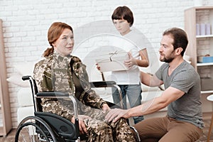 Woman veteran in wheelchair returned from army. The son and husband are happy to see her.