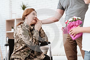 Woman veteran in wheelchair returned from army. The son and husband are happy to see her.