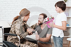 Woman veteran in wheelchair returned from army. The son and husband are happy to see her.