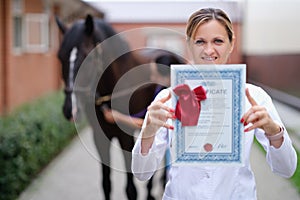 Woman veterinarian holding training certificate on horse background