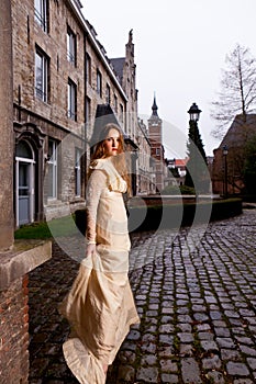 Woman in Victorian dress in a old city square in the evening in profile