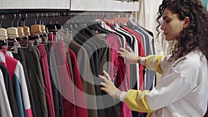 Woman is viewing clothing on sale in shop, moving hangers with pants and sweater