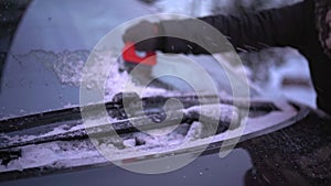 A woman vigorously scrapes the frozen windshield of her car.