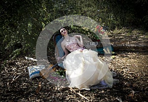 Woman in vintage couture dress reclining on rococo chair amidst an enchanted forest