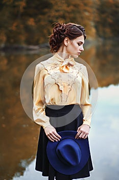 Woman with vintage hat near the river in autumn season