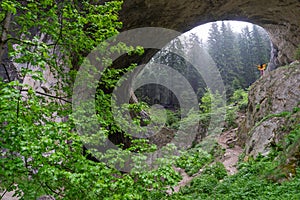 Woman visit geologic formation and open arms standing to the mysterious huge rock cave. Wonderful bridge in Bulgaria on tourist