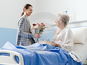 Woman visiting a senior patient and giving her flowers