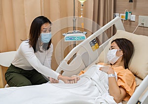 Woman visiting and take care female patient on bed at hospital. people must be wearing medical mask to prevention coronavirus photo