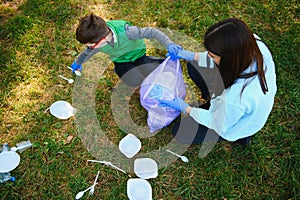 Woman volunteer and little boy picking up the plastic garbage and putting it in biodegradable trash-bag outdoors. Ecology,