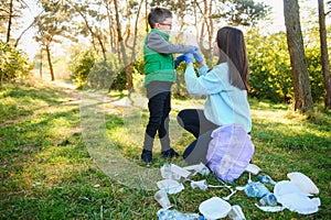 Woman volunteer and little boy picking up the plastic garbage and putting it in biodegradable trash-bag outdoors. Ecology,