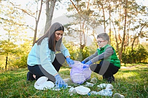 Woman volunteer and little boy picking up the plastic garbage and putting it in biodegradable trash-bag outdoors. Ecology,