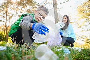 Woman volunteer and little boy picking up the plastic garbage and putting it in biodegradable trash-bag outdoors. Ecology,