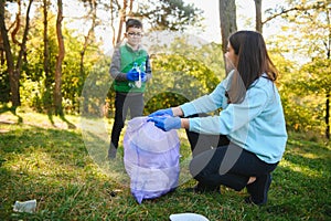 Woman volunteer and little boy picking up the plastic garbage and putting it in biodegradable trash-bag outdoors. Ecology,