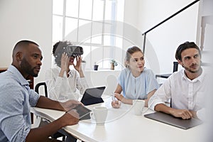 Woman in VR goggles at a desk with colleagues in an office