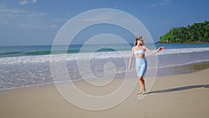 Woman in VR headset explores virtual tropics on beach, waves rolling nearby. Interactive tech adventure, touch gesture
