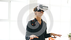 Woman in VR headset looking up and trying to touch objects in virtual reality at home indoors