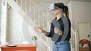 Woman in VR headset looking up and trying to touch objects in virtual reality at home indoors