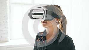 Woman in VR headset looking up and trying to touch objects in virtual reality in white room indoors