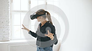 Woman in VR headset looking up and trying to touch objects in virtual reality in white room indoors