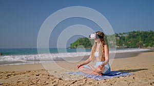 Woman in VR headset meditates on sandy beach, virtual reality transport to exotic locale for mindfulness. Tech offers