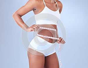 Woman, waist and weight loss with tape measure in underwear on a blue studio background. African, female person or young