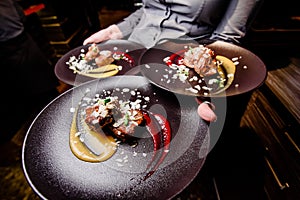 Woman waiter carries three plates of food. Meat steak garnished with two sauces on a dark plate