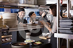 Woman waiter is giving order to chef cook on kitchen in restaurant.