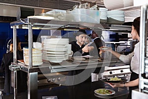 Woman waiter is giving order to chef cook on kitchen in restaurant.