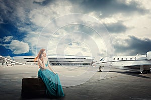 Woman waiting flight departure sitting on suitcase talking on phone