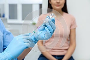 Woman waiting to get hepatitis vaccine at clinic. Doctor filling syringe from glass vial, closeup