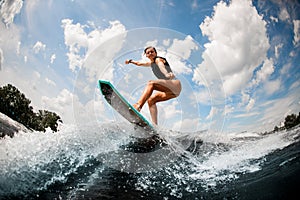 Woman wake surfer jumping up the splashing wave against on blue sky