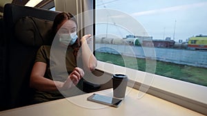 A woman wakes up on a train while traveling during a pandemic with a medical mask on her face. She picks up the phone
