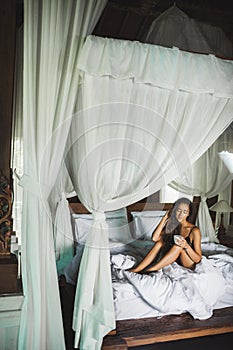 Woman waking up and enjoying morning coffee in bed with white canopy.