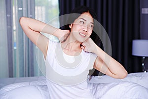 Woman waking up and hand raised on bed in bedroom