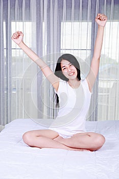 Woman waking up and hand raised on bed in bedroom