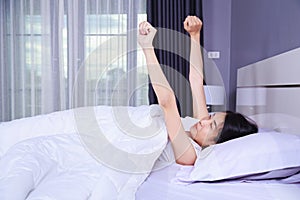 Woman waking up and hand raised on bed in bedroom