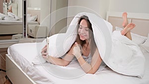 woman waking up in the morning in bed, using smartphone